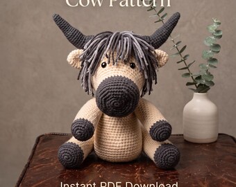 Könnte beinhalten: Ein gehäkeltes Hochlandrind-Spielzeug mit beigem Körper, dunkelgrauen Hörnern, Hufen und Schnauze sowie einer zotteligen grauen Mähne. Der Text lautet Crochet Highland Cow Pattern und Instant PDF Download. Es hat kleine schwarze Augen und runde Ohren.