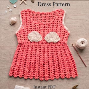 May include: A coral-colored sleeveless crochet dress featuring a scalloped hem and two cream-colored seashell appliqués on the bodice. The text reads Coral Cove Crochet Dress Pattern and Instant PDF Download, accompanied by buttons, a starfish, and yarn.