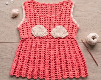 Könnte beinhalten: Ein korallenfarbenes, ärmelloses Häkelkleid mit gewelltem Saum und zwei cremefarbenen Muschelapplikationen am Oberteil. Der Text lautet Coral Cove Crochet Dress Pattern und Instant PDF Download, ergänzt durch Knöpfe, einen Seestern und Garn.