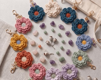 Könnte beinhalten: Handcrafted Crochet Flower Pendant Pattern Instant PDF Download. Eine Sammlung mehrfarbiger gehäkelter Blumen-Schlüsselanhänger mit goldenen Karabinerverschlüssen, verziert mit kleinen Perlen und verstreuten polierten Edelsteinen in verschiedenen Formen.