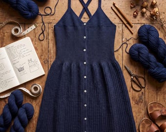 May include: A navy blue crochet ribbed button-down dress with a V-neckline and crisscross straps. The text reads Crochet Ribbed Navy Button-Down Dress Pattern and Instant PDF Download. The dress is surrounded by navy yarn, a notebook, and scissors.