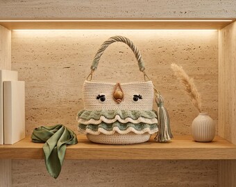 May include: A cream-colored crochet bucket bag featuring two sage green ruffled layers, a twisted rope handle, and a central wooden bead accent. The bag includes a matching sage green and cream tassel charm attached to the side with gold-tone hardware.