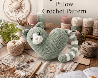 May include: A sage green heart-shaped cat pillow with a white muzzle, pink nose, and a striped tail. The text reads Sage Green Cat Pillow Crochet Pattern and INSTANT PDF DOWNLOAD. Surrounded by yarn balls, crochet hooks, and a pattern book.