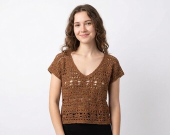 May include: A brown short-sleeved top featuring a V-neckline and an intricate crochet pattern with openwork details. The garment is constructed with a textured yarn, showcasing a repeating stitch design that creates a semi-sheer effect throughout.