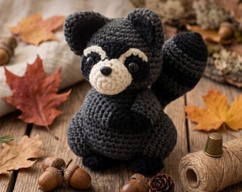 May include: A dark gray and cream crocheted raccoon amigurumi with black accents, featuring the text Amigurumi Raccoon Crochet Pattern and Instant PDF Download. The raccoon has a striped tail, dark eyes, and a round snout, crafted with yarn.