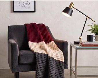 Könnte beinhalten: Eine Häkelanleitung für eine Waffelstrickdecke mit einem Color-Block-Design in Dunkelburgunder, Creme und Dunkelgrau. Der Text Waffle Knit Blanket Crochet Pattern und Instant PDF Download ist auf dem Bild des fertigen Textils zu sehen.