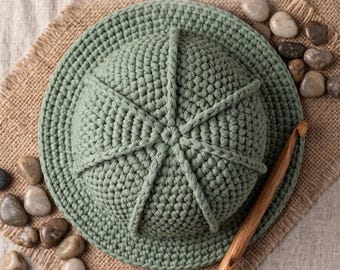 Könnte beinhalten: Ein salbeigrüner gehäkelter Hut mit einer strukturierten, gerippten Krone und einer breiten Krempe, begleitet von einer Häkelnadel aus Holz. Der Text Evergreen Handmade Boho Hat Crochet Pattern und Instant PDF Download ist sichtbar.