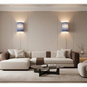 May include: A modern living room featuring a beige sectional sofa with brown accents, a glass coffee table, and a cream-colored armchair. Two blue wall sconces illuminate the space, creating a warm and inviting atmosphere.