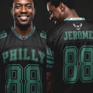 May include: A black sports jersey featuring the word PHILLY and the number 88 in teal with black outlines on the front. The back displays the name JEROME, the number 88, an eagle graphic, and the word Philadelphia on the collar in teal and white.
