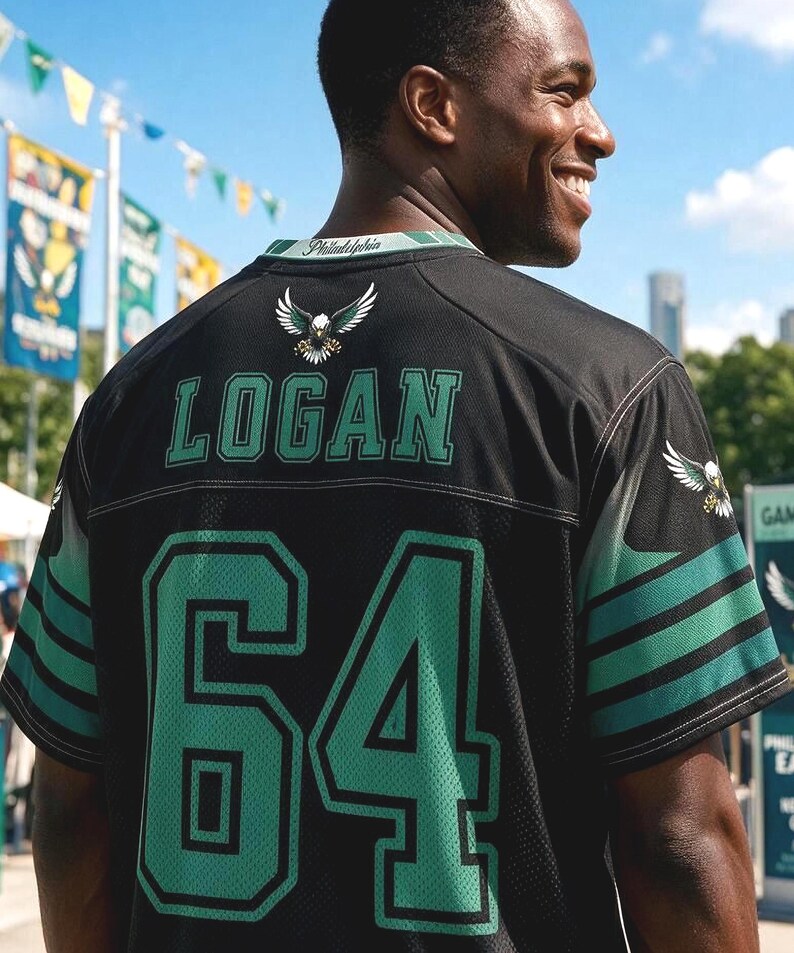 May include: A black sports jersey featuring the name LOGAN and the number 64 in green with black outlines on the back. The jersey includes an eagle graphic on the upper back and sleeves, with the word Philadelphia printed on the collar trim.