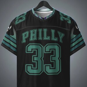 May include: A black short-sleeve jersey with a V-neck collar. The front features the word PHILLY in teal block letters above the large number 33 in teal with black outlines. Teal numbers 33 appear on the shoulders, and teal stripes accent the sleeves.