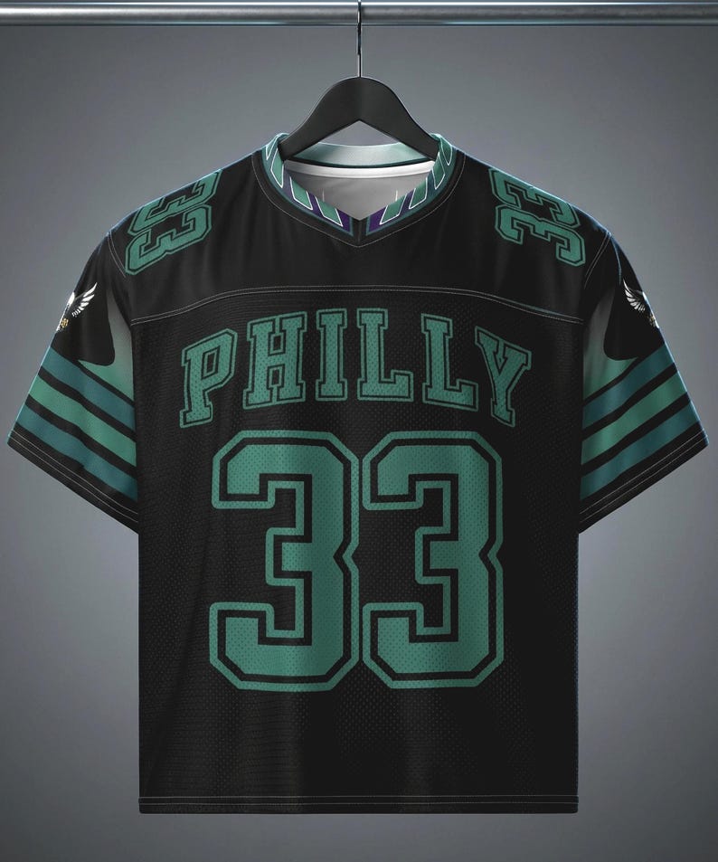 May include: A black short-sleeve jersey with a V-neck collar. The front features the word PHILLY in teal block letters above the large number 33 in teal with black outlines. Teal numbers 33 appear on the shoulders, and teal stripes accent the sleeves.