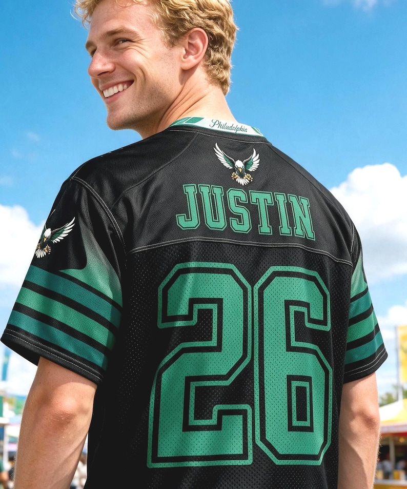 May include: A black sports jersey featuring the name JUSTIN and the number 26 in green with black outlines. The back of the jersey displays an eagle emblem, green and black sleeve stripes, and the word Philadelphia printed on the inner collar.