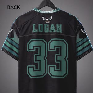 May include: A black sports jersey featuring the name LOGAN and the number 33 in green with black outlines. The shirt includes an eagle graphic, the text Philadelphia on the collar, and green and black striped patterns on the short sleeves.