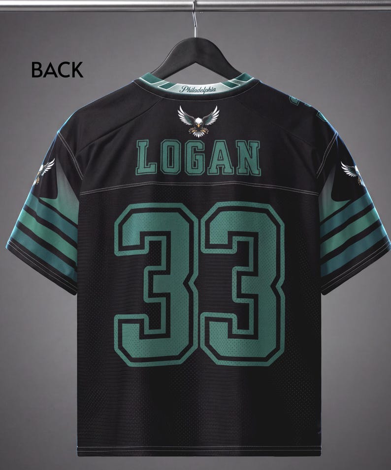 May include: A black sports jersey featuring the name LOGAN and the number 33 in green with black outlines. The shirt includes an eagle graphic, the text Philadelphia on the collar, and green and black striped patterns on the short sleeves.