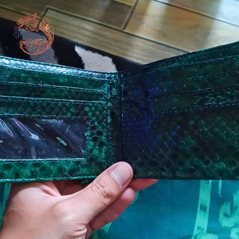 May include: Open green snakeskin wallet with multiple card slots and a clear ID window. The wallet is held open, showcasing the interior design and texture of the exotic leather. The wallet is a bi-fold style.
