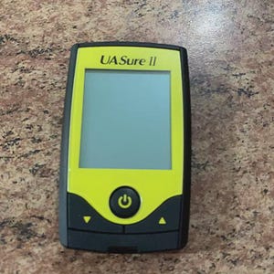 May include: A handheld device with a black and yellow color scheme. The device has a rectangular screen and a power button. The text "UA Sure II" is printed at the top. The device is likely a medical or diagnostic tool.