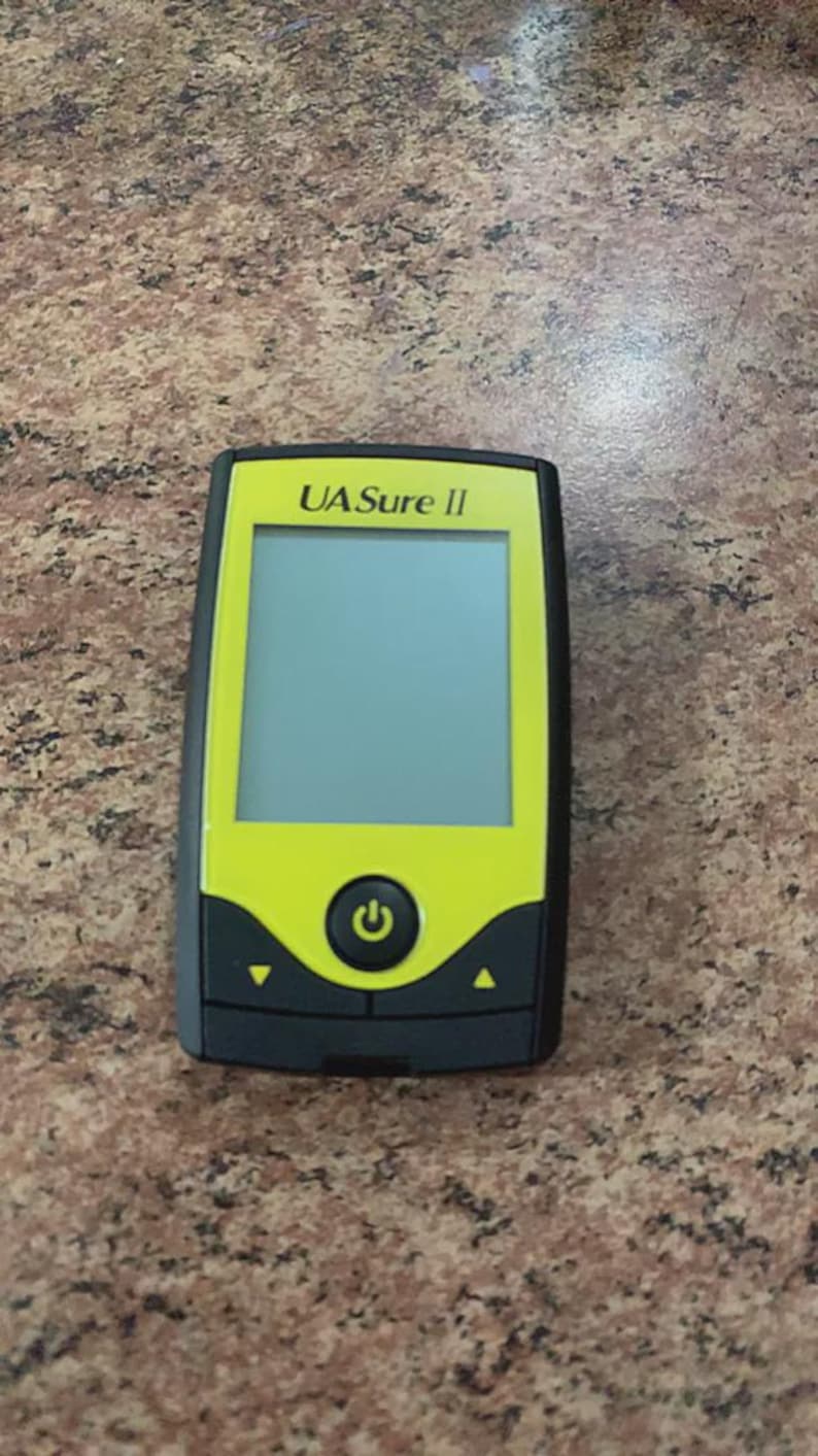 May include: A handheld device with a black and yellow color scheme. The device has a rectangular screen and a power button. The text "UA Sure II" is printed at the top. The device is likely a medical or diagnostic tool.