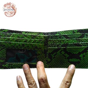 May include: Open green and black snakeskin bi-fold wallet. The wallet has multiple card slots and a clear ID window. The wallet is open, displaying the interior. The wallet is made of a snakeskin material.