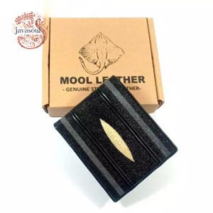 Op de afbeelding: Zwart leren portemonnee met een accent van roggenhuid. De portemonnee heeft grijze strepen en een lichtbeige roggenhuid ontwerp. De doos achter de portemonnee heeft de tekst "MOOL LEATHER - GENUINE ST..." en een roggenillustratie.