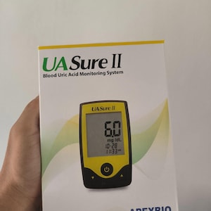 May include: A white box with the text "UA Sure II Blood Uric Acid Monitoring System" and a yellow and black blood uric acid monitor. The monitor displays a reading of 6.0 mg/dL and the time. The box is labeled "BASIC KIT Suitable For Self-testing."
