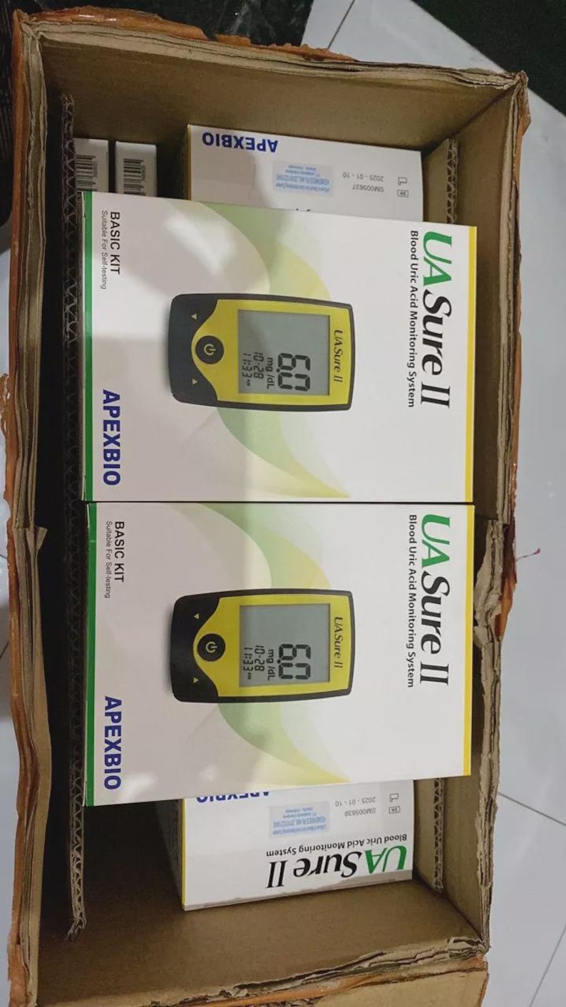 May include: A cardboard box containing multiple boxes of the UA Sure II Blood Uric Acid Monitoring System. Each box features a yellow and black meter displaying a reading of 6.0 mg/dL. The boxes also display the ApexBio logo.
