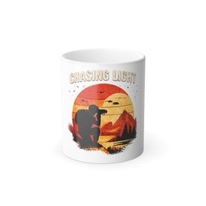 May include: White ceramic mug with the text "CHASING LIGHT" above a graphic of a photographer silhouetted against a sunset over mountains. The design features shades of orange, red, and brown.