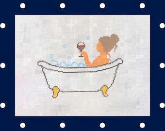 May include: A cross-stitch pattern on white fabric featuring a person with brown hair sitting in a white clawfoot bathtub filled with blue bubbles. The person is holding a glass of red wine. The text pickle pop stitches appears in the bottom right.