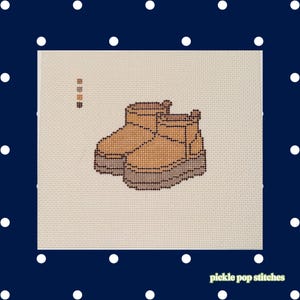 Könnte beinhalten: Ein Kreuzstichmuster auf hellem Stoff mit einem Paar hellbrauner Stiefeletten mit dicken dunkelbraunen Sohlen. Das Design enthält eine kleine Farbpalette oben links und den Text pickle pop stitches in der unteren rechten Ecke.