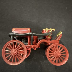 Peut inclure: Une voiture jouet miniature de style antique dans les tons de rouge, noir et or. La voiture jouet présente des roues à rayons, un moteur détaillé et une carrosserie en forme de voiture. Le design général évoque une esthétique vintage.