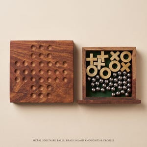 May include: A wooden game set featuring a square board with circular indentations for solitaire and a matching box containing brass X and O game pieces alongside numerous small silver-colored metal balls. Text reads: METAL SOLITAIRE BALLS, BRASS INLAID KNOUGHTS & CROSSES.