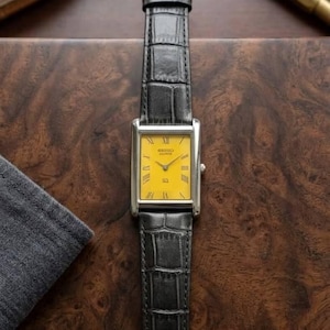 May include: A rectangular wristwatch with a bright yellow dial, silver-tone case, and black leather strap featuring a crocodile-embossed texture. The watch face displays black Roman numeral hour markers, thin silver hands, and the text Seiko Quartz.