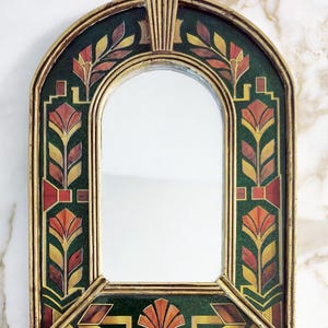 May include: An arched wall mirror featuring a gold-toned frame and a decorative border with a dark green background. The border is adorned with repeating floral-inspired patterns in shades of orange, yellow, and deep red, creating a symmetrical design.