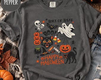 May include: A charcoal gray short-sleeve t-shirt featuring a colorful Halloween graphic print. The design includes a ghost, black cat, pumpkins, skulls, a witch hat, spider web, and candy. The text reads TRICK OR TREAT, BOO, and HAPPY HALLOWEEN.