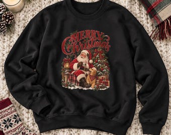 May include: A black long-sleeve sweatshirt featuring a graphic print of Santa Claus sitting with a golden dog in front of a Christmas tree. The text Merry Christmas is printed in red above the illustration, which includes a lantern and gifts.