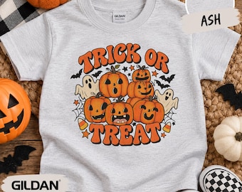May include: An ash gray short-sleeve t-shirt featuring a graphic print with the text TRICK OR TREAT in orange. The design includes a stack of five orange jack-o'-lanterns, two white ghosts, black bats, and spider webs on a light gray background.