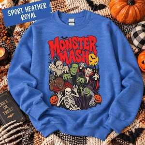 May include: A sport heather royal blue sweatshirt featuring a graphic print with the text Monster Mash and illustrations of a mummy, Frankenstein's monster, a vampire, a werewolf, a skeleton, and a witch surrounded by pumpkins and bats.