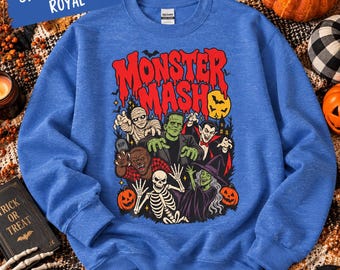 May include: A sport heather royal blue sweatshirt featuring a graphic print with the text Monster Mash and illustrations of a mummy, Frankenstein's monster, a vampire, a werewolf, a skeleton, and a witch surrounded by pumpkins and bats.