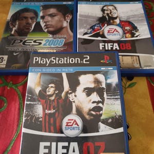 May include: Three PlayStation 2 video game cases. The games are "PES 2008", "FIFA 08", and "FIFA 07". The cases feature images of football players and the EA Sports logo. The games are in blue cases.