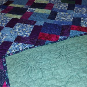 May include: A close-up of a teal blue quilted fabric with a floral pattern. The fabric is stitched with a decorative pattern of flowers.
