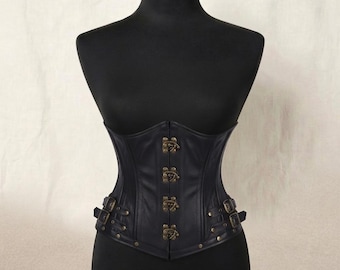 May include: A black corset featuring a front closure with four antique brass-toned metal clasps. The garment includes decorative side straps with matching brass-toned buckles and studs, providing a structured fit around the waist area.