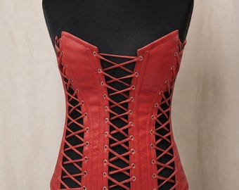 May include: A red strapless corset top featuring a front lace-up closure with silver-toned metal eyelets and matching side lace-up panels. The garment is constructed from a smooth material and is displayed on a black mannequin torso.