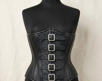 May include: A black corset featuring a front closure with five horizontal straps, each secured by a silver-toned metal buckle. The garment is constructed with vertical panels and has a straight neckline, designed to fit snugly around the torso.