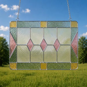 May include: A rectangular stained glass panel featuring a grid of clear textured glass panes, accented by three central pink diamond shapes, green corner sections, and small yellow square inserts, all held together by silver metal lead lines.