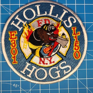 Puede incluir: Parche bordado con fondo azul y borde blanco. El parche presenta el texto "HOLLIS" y "HOGS" en blanco, con "E301" y "L150" en rojo. Un jabalí de dibujos animados con un hacha está en el centro, con el texto "NY" debajo.