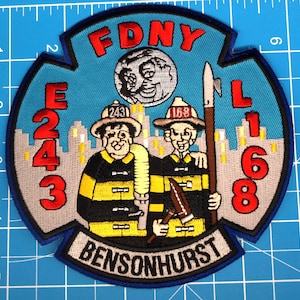 May include: Embroidered FDNY patch with a blue background, featuring two firefighters, the text "FDNY", "E 243", "L 168", and "BENSONHURST". The patch is approximately 10 cm in diameter.