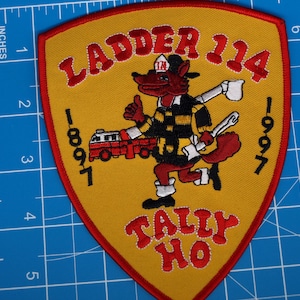 Puede incluir: Parche bordado con forma de escudo, con un zorro de dibujos animados con uniforme de bombero. El parche tiene el texto "LADDER 114 TALLY HO" y los años 1897 y 1997. El parche es amarillo con detalles en rojo y negro, y mide unos 10 cm de alto.