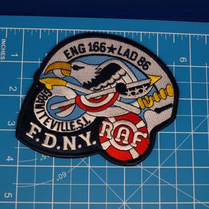 May include: Embroidered patch featuring a stylized eagle with crossed axes, a red and white life preserver, and the text "ENG 166 LAD 86" and "GRANITEVILLE S.I. F.D.N.Y. RAF". The patch is approximately 3 inches wide.