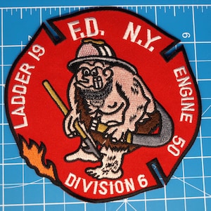 May include: A red, embroidered patch featuring a cartoon firefighter with a beard, holding tools. The patch includes the text "LADDER 19," "E.D. N.Y.," "ENGINE 50," and "DIVISION 6." A flame design is on the lower left.