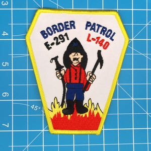 May include: Embroidered patch with a yellow border and a white interior. The patch features a cartoon figure in a black hat and red shirt, holding tools. Text at the top reads "BORDER PATROL" and "L-140" and "E-291". The bottom has flames.